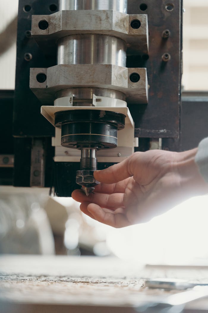 Detailed shot of a CNC machine spindle being adjusted by a human hand in a workshop setting.